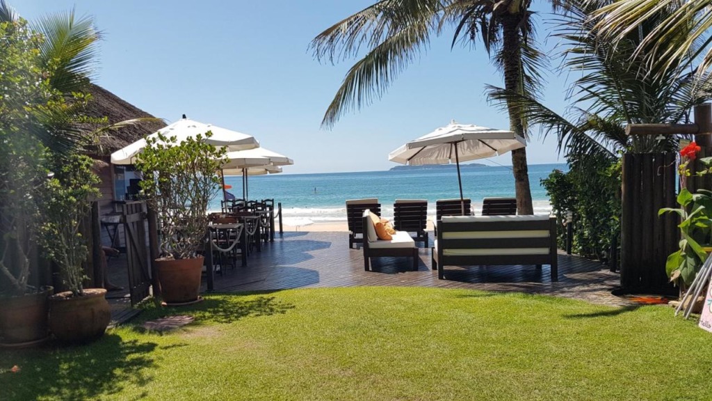 Jardim com deck de madeira, espreguiçadeiras e sombreiros com acesso para a praia. Pousadas pé na areia em Bombinhas.