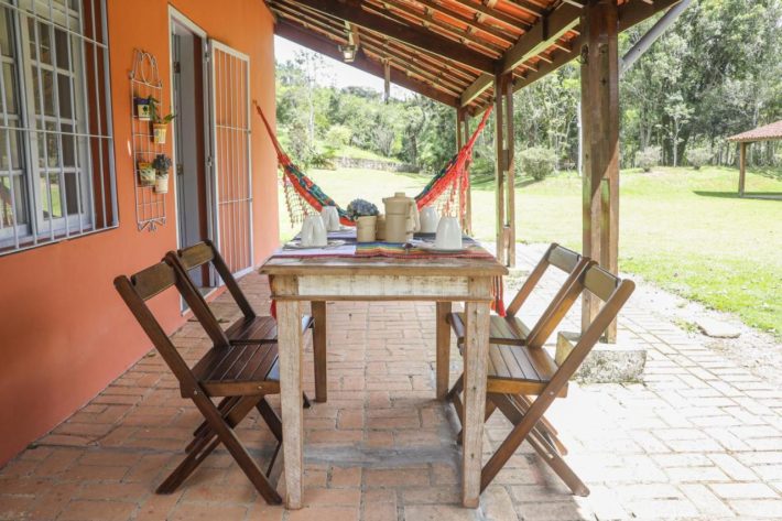 Varanda com mesa de madeira com café da manhã e rede.