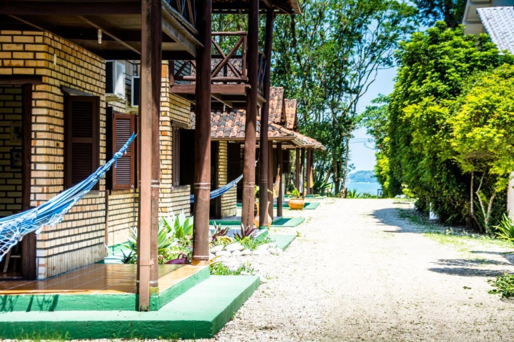 Chalés em pousadas pé na areia em Bombinhas, com mar ao fundo do caminho de terra.