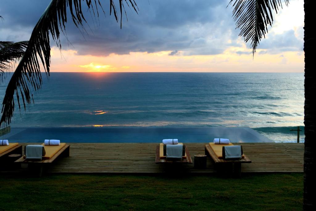 Vista panorâmica do mar da piscina de borda infinita em deck de madeira com espreguiçadeiras. Pôr-do-sol em pousadas para casal perto de Maceió.