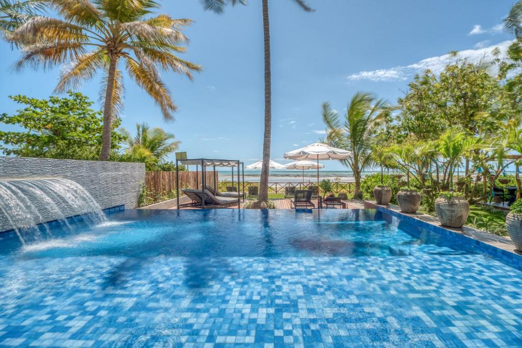 Piscina ao ar livre com chafariz, espreguiçadeiras em deck de madeira e vista para o mar.