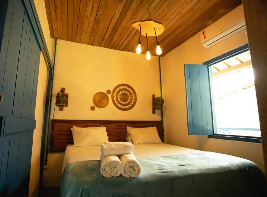 Cama de casal em quarto compacto com decoração rústica elegante, janelas e portas em madeira azuis.