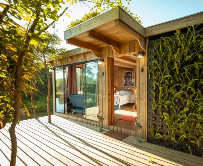 Fachada de cabana de madeira, com deck em madeira e parede verde, em pousadas na praia da Ferrugem.