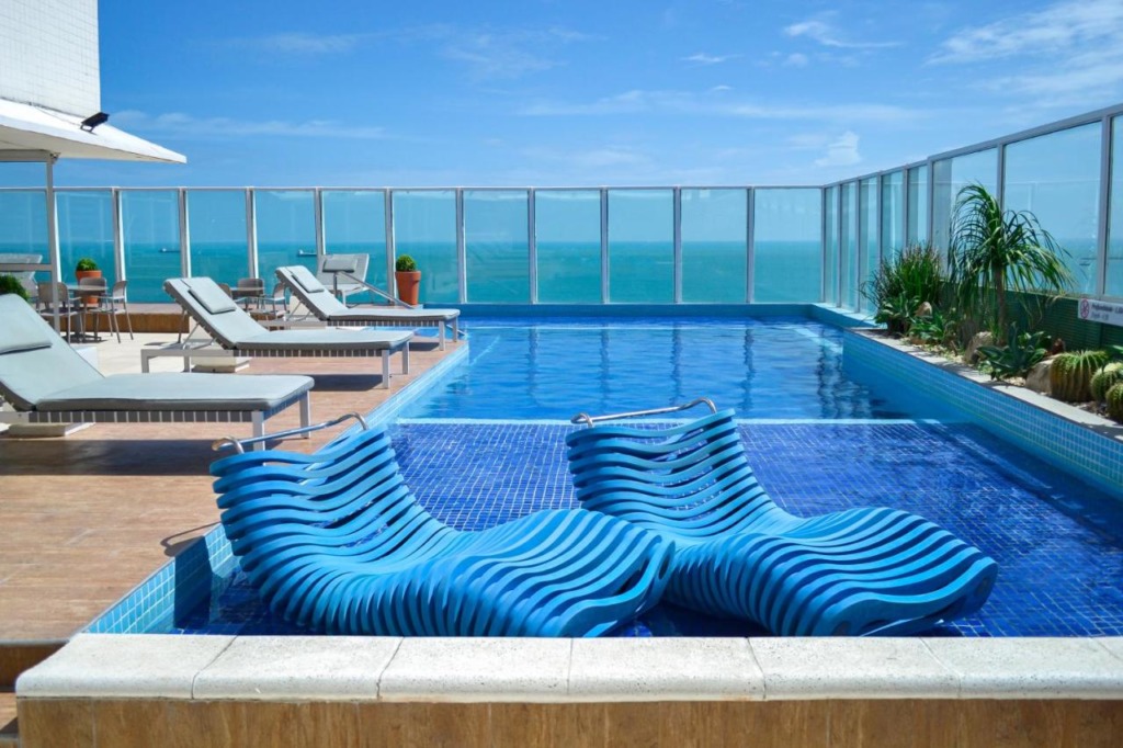 Piscina no alto com vista para o mar, tem espreguiçadeiras.