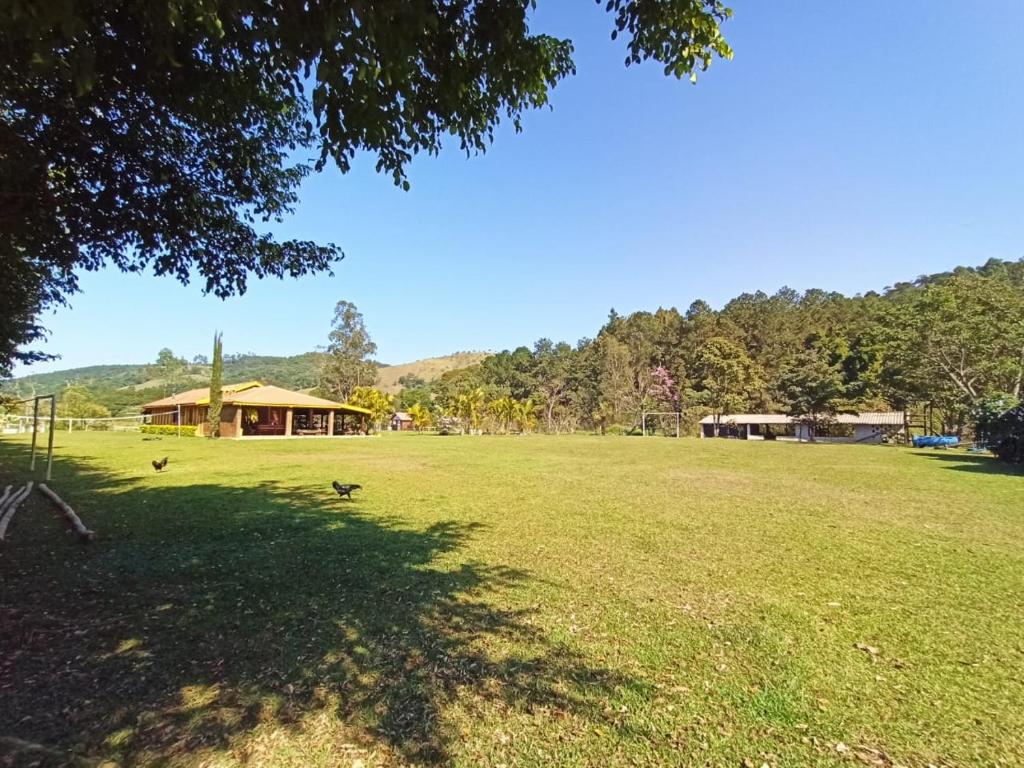 Ampla área com gramado, árvores ao fundo, um pouco de morros verdes e uma casa com varanda. 