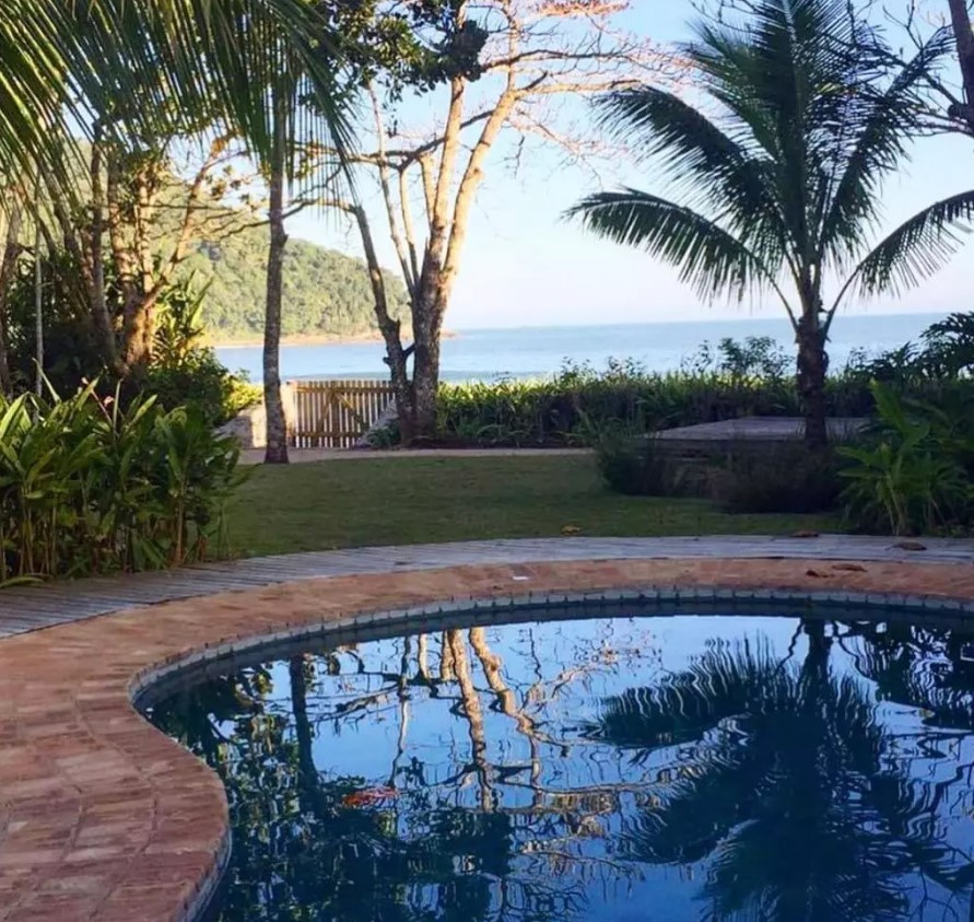 Piscina em jardim com vista para o mar.