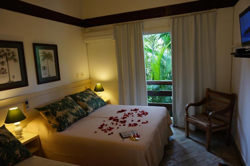 Suíte tripla com varanda, na cama de casal flores e cadeira no canto do quarto. Pousadas perto da praia da Baleia.