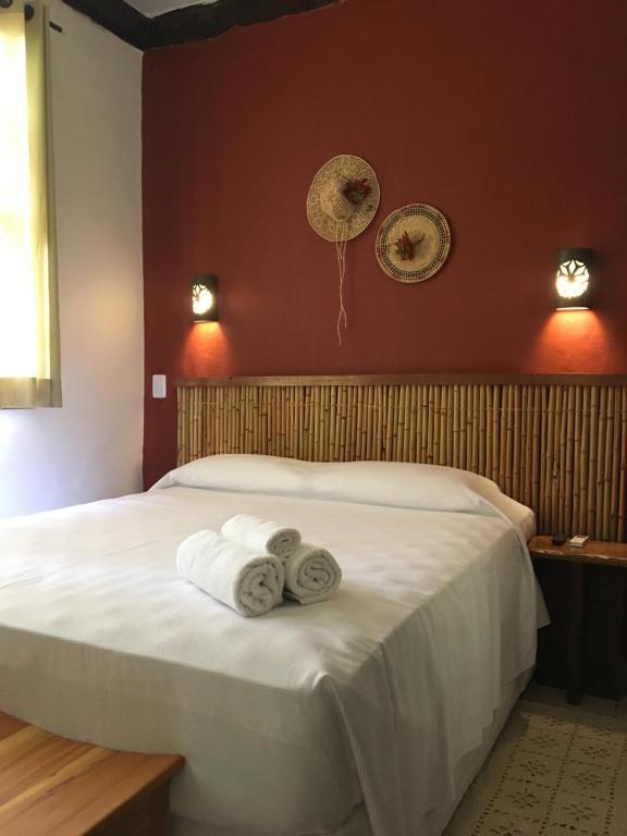 Quarto com cama de casal, toalhas rolinhos na cama e parede vermelha com detalhes em bambu. Em pousadas perto da praia da baleia.